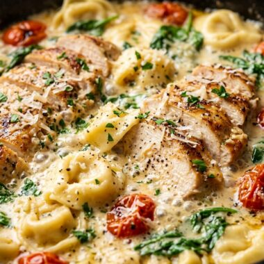 Ultra close-up macro of creamy garlic herb chicken and cheese tortellini simmering in parmesan sauce