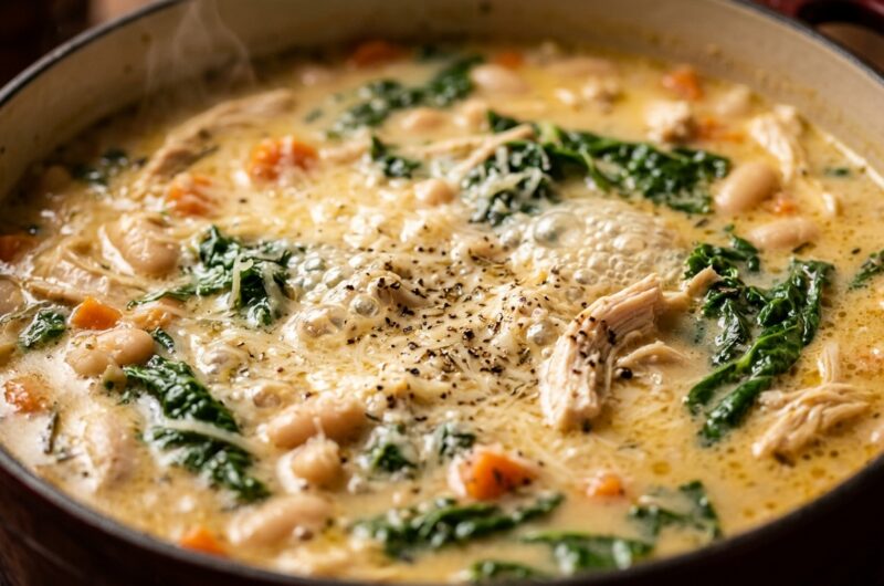 Ultra close-up macro of creamy Tuscan white bean and chicken soup simmering with kale in a Dutch oven