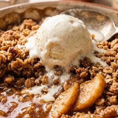 Ultra close-up macro of warm baked homemade apple crisp with golden brown oat streusel crumble and melting vanilla ice cream