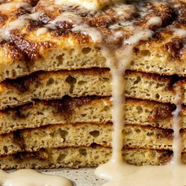Ultra close-up macro of a thick fluffy stack of cinnamon roll pancakes with cascading cream cheese glaze and caramelized cinnamon swirls