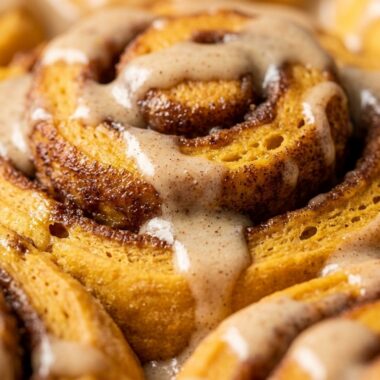 Ultra close-up macro of fluffy pumpkin cinnamon rolls with dripping molten maple cream cheese icing