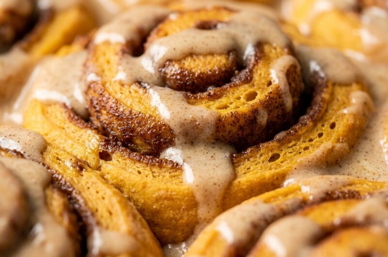 Ultra close-up macro of fluffy pumpkin cinnamon rolls with dripping molten maple cream cheese icing