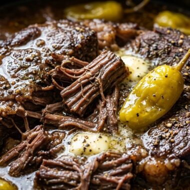 Ultra close-up macro of slow cooker Mississippi pot roast with tender shredded beef, golden pepperoncinis, and rich buttery au jus gravy